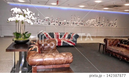 sophisticated indoor lounge area with union jack pattern sofa and relaxed atmosphere featuring leather armchair and coffee table with cityscape wall art and flower arrangement. sophisticated indoor lounge area with union jack pattern sofa and relaxed atmosphere featuring leather armchair and coffee table with cityscape wall art and flower arrangement. 142387877