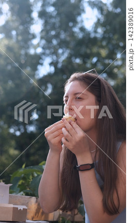 woman eating cake outdoors in a relaxed and happy setting with sunglasses on head and smartwatch, side view close-up with brown hair and wooden surface, brown and white colors, food and lfe. woman eating cake outdoors in a relaxed and happy setting with sunglasses on head and smartwatch, side view close-up with brown hair and wooden surface, brown and white colors, food and lfe. 142389016