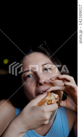 woman eating sandwich in dark setting with contentment close-up hand bread filling food lifestyle blue brown commercial natural light clean copy space editorial educational visual story web. 142389017