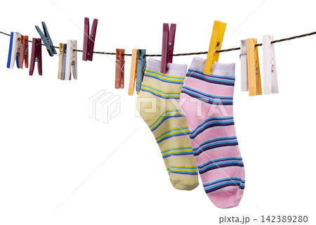 Two striped socks, one yellow and one pink, hang on a clothesline clipped by various clothespins. Two striped socks, one yellow and one pink, hang on a clothesline clipped by various clothespins. 142389280