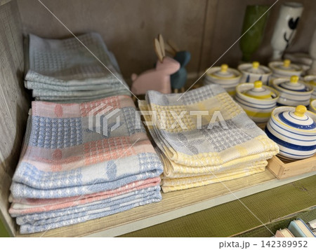 Towels neatly stacked on wooden shelf with ceramic jars and bunny figurine in cozy kitchen setting Towels neatly stacked on wooden shelf with ceramic jars and bunny figurine in cozy kitchen setting 142389952