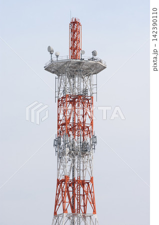 A tall industrial telecommunications tower with an orange and white lattice structure in a pale overcast sky 142390110