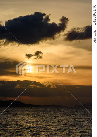 A dramatic sunset over water, featuring a partially obscured sun and large dark cloud formation in the upper part of the image 142390140