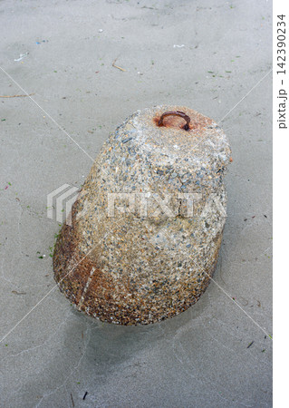 A weathered conical stone resting on a wet sand beach, with rusted metal embedded at its top A weathered conical stone resting on a wet sand beach, with rusted metal embedded at its top 142390234
