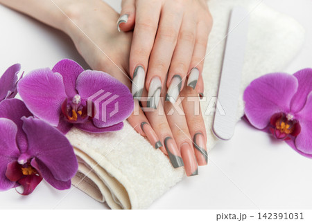 Woman receiving manicure treatment with orchids and nail file Woman receiving manicure treatment with orchids and nail file 142391031