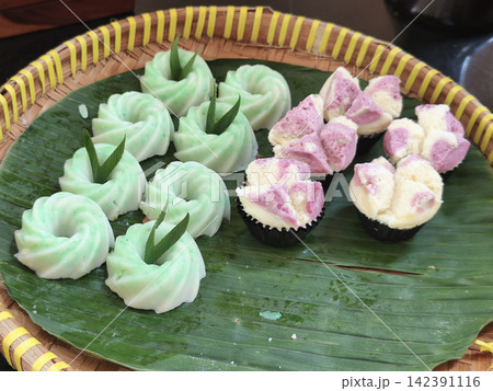 Traditional Indonesian sweet snacks (kue basah) shaped like green and pink flowers served on a banana leaf in a woven bamboo basket Traditional Indonesian sweet snacks (kue basah) shaped like green and pink flowers served on a banana leaf in a woven bamboo basket 142391116