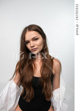 Young woman looking directly at the camera, showing a confident and natural expression, with long brown hair Young woman looking directly at the camera, showing a confident and natural expression, with long brown hair 142391632
