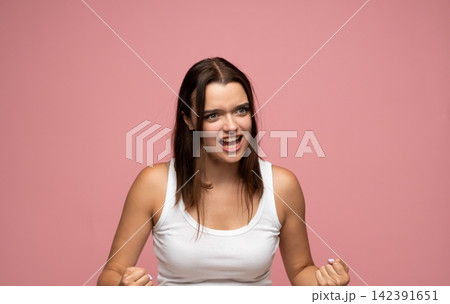 Young woman shouting and expressing anger, frustration, and aggression with clenched fists on a solid pink background Young woman shouting and expressing anger, frustration, and aggression with clenched fists on a solid pink background 142391651