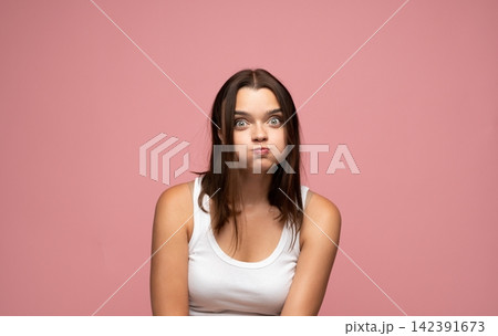 Young woman making a goofy face, puffing cheeks and widening eyes. Expressing humor, silliness, and playful emotion Young woman making a goofy face, puffing cheeks and widening eyes. Expressing humor, silliness, and playful emotion 142391673