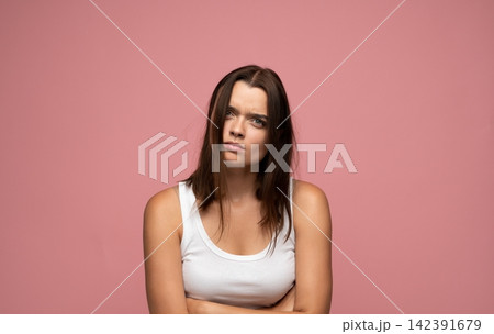 Woman expressing annoyance and disbelief, arms crossed, feeling upset and skeptical against a pink background Woman expressing annoyance and disbelief, arms crossed, feeling upset and skeptical against a pink background 142391679