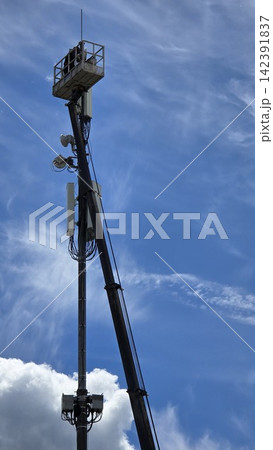 A male technician wearing a helmet works on a tall telecommunications tower from a heavy duty aerial lift. 142391837