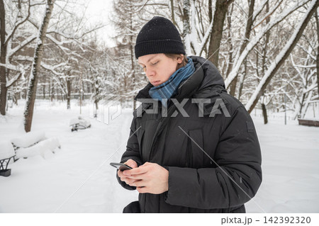 Young man using smartphone outdoors during winter snowfall Young man using smartphone outdoors during winter snowfall 142392320