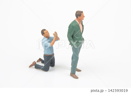 Miniature figures act out a scene with one figure kneeling and the other standing in a simple setup Miniature figures act out a scene with one figure kneeling and the other standing in a simple setup 142393019