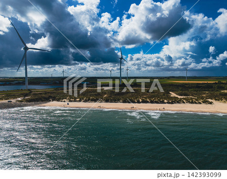 High angle wide horizontal aerial drone photograph of wind turbines, sandy beach, coastal sand dunes, and North Sea waves in Neeltje Jans, Zeeland, Netherlands on sunny summer day High angle wide horizontal aerial drone photograph of wind turbines, sandy beach, coastal sand dunes, and North Sea waves in Neeltje Jans, Zeeland, Netherlands on sunny summer day 142393099