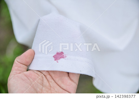 hand holding a white shirt showing a red lipstick or cosmetics stain hand holding a white shirt showing a red lipstick or cosmetics stain 142398377