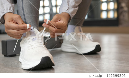 A woman ties her shoelaces ready to run at the gym. A woman ties her shoelaces ready to run at the gym. 142399293