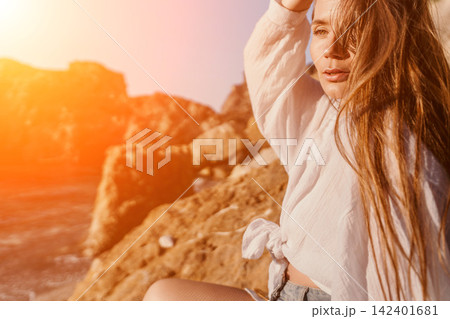 Woman sunset coast Young woman in white shirt sitting on rocky cliffs during golden hour for summer travel Woman sunset coast Young woman in white shirt sitting on rocky cliffs during golden hour for summer travel 142401681
