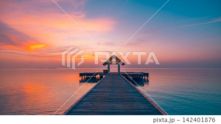 Breathtaking wooden jetty leading glowing pastel dusk calm azure Maldives lagoon warm reflected sky. Luxury travel honeymoon paradise scenic. Exotic getaway wall art decor 142401876