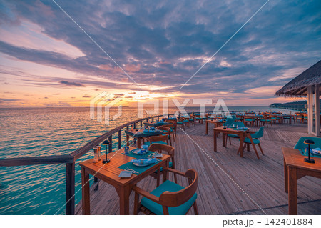 Romantic overwater dining terrace glowing sunset vivid azure Maldives lagoon set tables warm horizon. Luxury honeymoon travel paradise scenic. Exotic couples getaway wall art decor Romantic overwater dining terrace glowing sunset vivid azure Maldives lagoon set tables warm horizon. Luxury honeymoon travel paradise scenic. Exotic couples getaway wall art decor 142401884