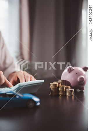Calculator, piggy bank, stacked coins, and blue car model depict vehicle budgeting, saving for transportation, auto purchase planning, financing decisions, household expenses, and future goals. Calculator, piggy bank, stacked coins, and blue car model depict vehicle budgeting, saving for transportation, auto purchase planning, financing decisions, household expenses, and future goals. 142402244