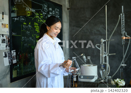 Young Asian Female Scientist in White Lab Coat Working with Distillation Equipment in Laboratory Young Asian Female Scientist in White Lab Coat Working with Distillation Equipment in Laboratory 142402320