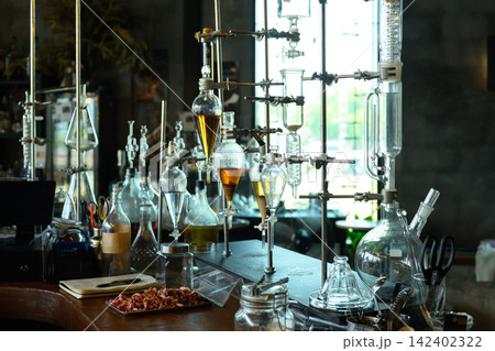 Artisan Perfume Distillation Laboratory with Glass Apparatus and Amber Essential Oils on Wooden Workbench Artisan Perfume Distillation Laboratory with Glass Apparatus and Amber Essential Oils on Wooden Workbench 142402322