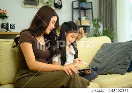 Asian Mother and Daughter Using Digital Tablet Together on Sofa at Home Asian Mother and Daughter Using Digital Tablet Together on Sofa at Home 142402371