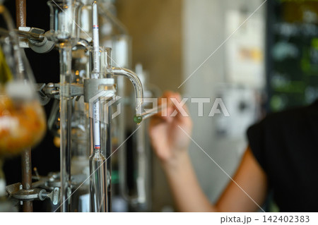 Scientist Collecting Essential Oil Drop from Glass Distillation Apparatus in Laboratory 142402383