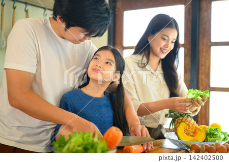 Happy Family Cooking Together in Kitchen, Parents Teaching Daughter to Prepare Healthy Vegetables at Home 142402500