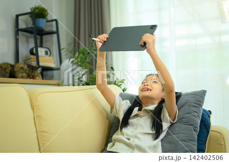 Happy Asian Girl Lying on Sofa Using Digital Tablet with Stylus Pen at Home Happy Asian Girl Lying on Sofa Using Digital Tablet with Stylus Pen at Home 142402506