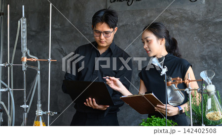 Two Asian Scientists Reviewing Research Data in Modern Botanical Laboratory with Glassware and Herbs 142402508