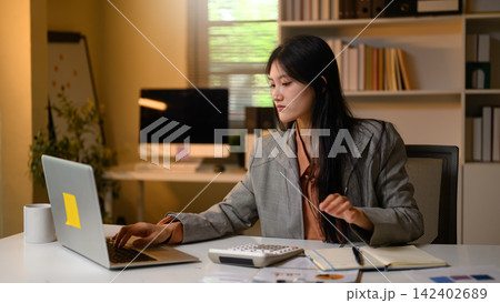 Young Asian Businesswoman Working on Laptop at Office Desk with Calculator and Documents 142402689
