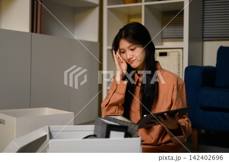 Young Asian Woman Packing Personal Belongings in Office Box After Job Loss, Looking Sad and Thoughtful Young Asian Woman Packing Personal Belongings in Office Box After Job Loss, Looking Sad and Thoughtful 142402696