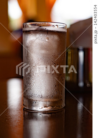 暖かな逆光に照らされた結露のついた冷たい水のグラス 暖かな逆光に照らされた結露のついた冷たい水のグラス 142403554