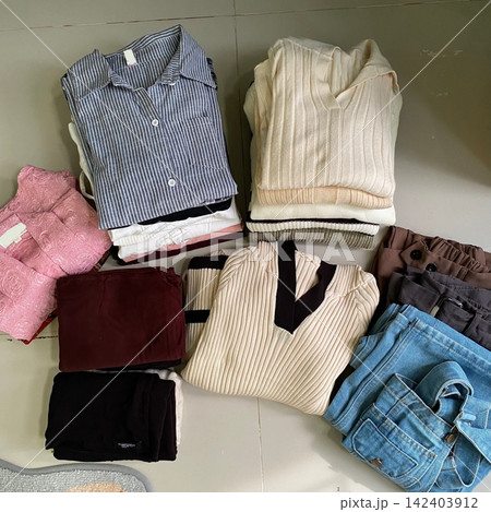 Stack of neatly folded clothes in various colors and fabrics, showing layered textures, soft materials, and stylish casual outfits prepared for daily wear, highlighting a trendy OOTD concept in detail Stack of neatly folded clothes in various colors and fabrics, showing layered textures, soft materials, and stylish casual outfits prepared for daily wear, highlighting a trendy OOTD concept in detail 142403912