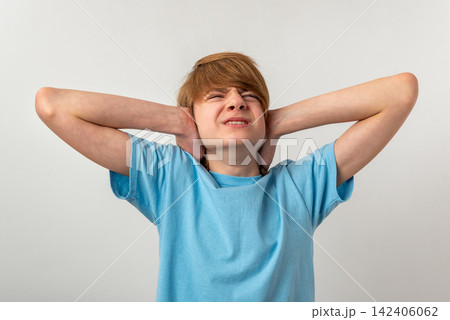Young boy experiencing discomfort and annoyance, covering his ears with hands to block out unpleasant, excessive sound and showing an expression of irritation 142406062