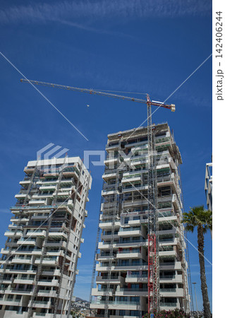 Tall red construction crane builds modern residential glass skyscrapers in an urban setting Tall red construction crane builds modern residential glass skyscrapers in an urban setting 142406244