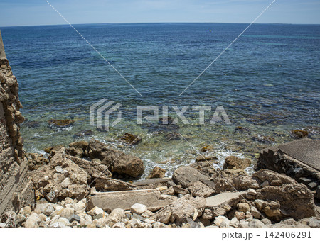 Coastal view of rugged rocky shore with turquoise sea water and distant city skyline along the bay 142406291