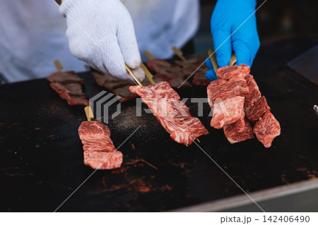 Wagyu beef skewers grilling on hot teppanyaki teppan iron plate, premium Japanese marbled meat on wooden sticks, traditional street food festival, Tokyo, Japan, market with local vendor stalls cooking Wagyu beef skewers grilling on hot teppanyaki teppan iron plate, premium Japanese marbled meat on wooden sticks, traditional street food festival, Tokyo, Japan, market with local vendor stalls cooking 142406490