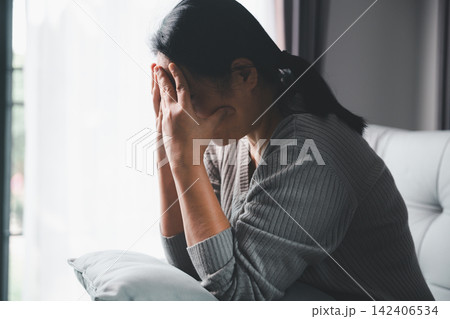 Stressed adult woman sitting on a sofa with her face covered by both hands, expressing anxiety, emotional exhaustion, burnout, sadness, and feeling overwhelmed by personal problems. Stressed adult woman sitting on a sofa with her face covered by both hands, expressing anxiety, emotional exhaustion, burnout, sadness, and feeling overwhelmed by personal problems. 142406534