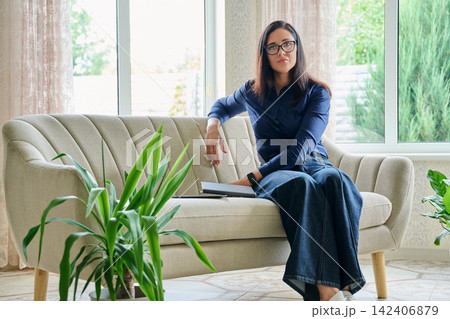 Thoughtful businesswoman leaning on sofa looking at camera during work break at home office Thoughtful businesswoman leaning on sofa looking at camera during work break at home office 142406879