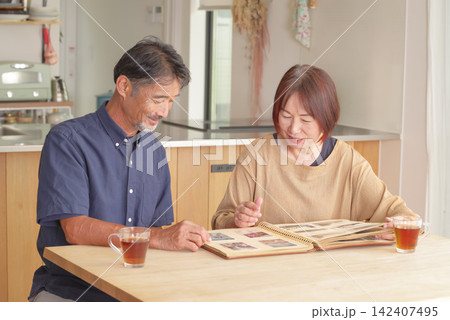 昔の写真を見ながら思い出を語る熟年夫婦 昔の写真を見ながら思い出を語る熟年夫婦 142407495