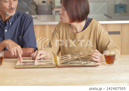 昔の写真を見ながら思い出を語る熟年夫婦 昔の写真を見ながら思い出を語る熟年夫婦 142407505