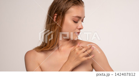 Young woman applying moisturizing cream to shoulder, enhancing skin health and body care routine 142407812