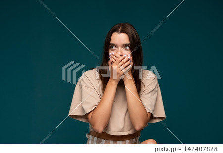 Young woman covering mouth with hands, feeling fear, expressing shock, keeping a secret, feeling afraid to speak Young woman covering mouth with hands, feeling fear, expressing shock, keeping a secret, feeling afraid to speak 142407828