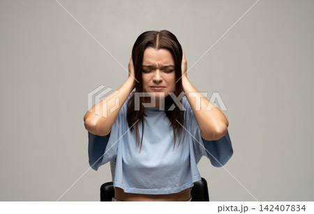 Young woman covering ears with hands, experiencing headache or stress from loud noise, suffering migraine symptoms Young woman covering ears with hands, experiencing headache or stress from loud noise, suffering migraine symptoms 142407834