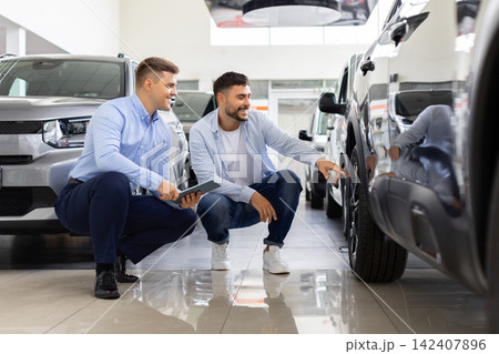 Salesman and customer crouching to inspect car tire and wheel closely together 142407896