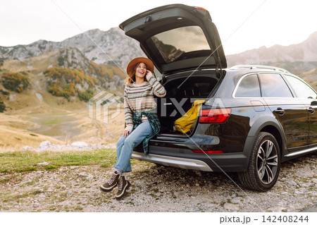 Young woman enjoying autumn nature while sitting in the trunk of her car during a trip. Road trip. 142408244