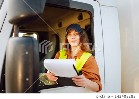 Woman truck driver steering wheel inside lorry cabin with clipboard. People and transportation Woman truck driver steering wheel inside lorry cabin with clipboard. People and transportation 142408288