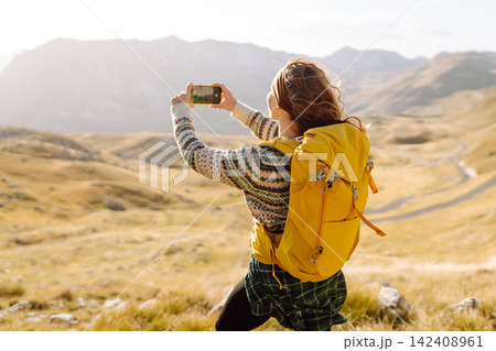 A young woman captures a moment while hiking in a mountainous landscape during golden hour 142408961